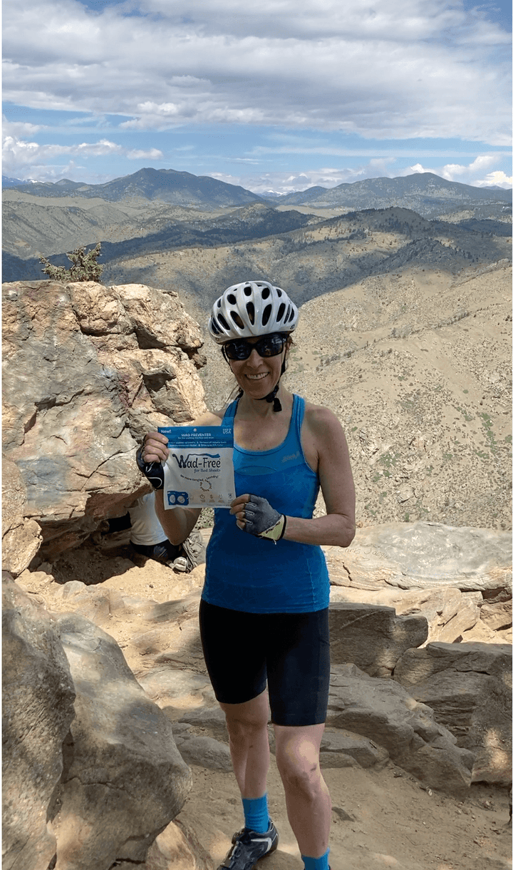 Wad-Free Inventor Cyndi Bray in bicycle clothes and helmet holding up a package of Wad-Free in an mountain scene