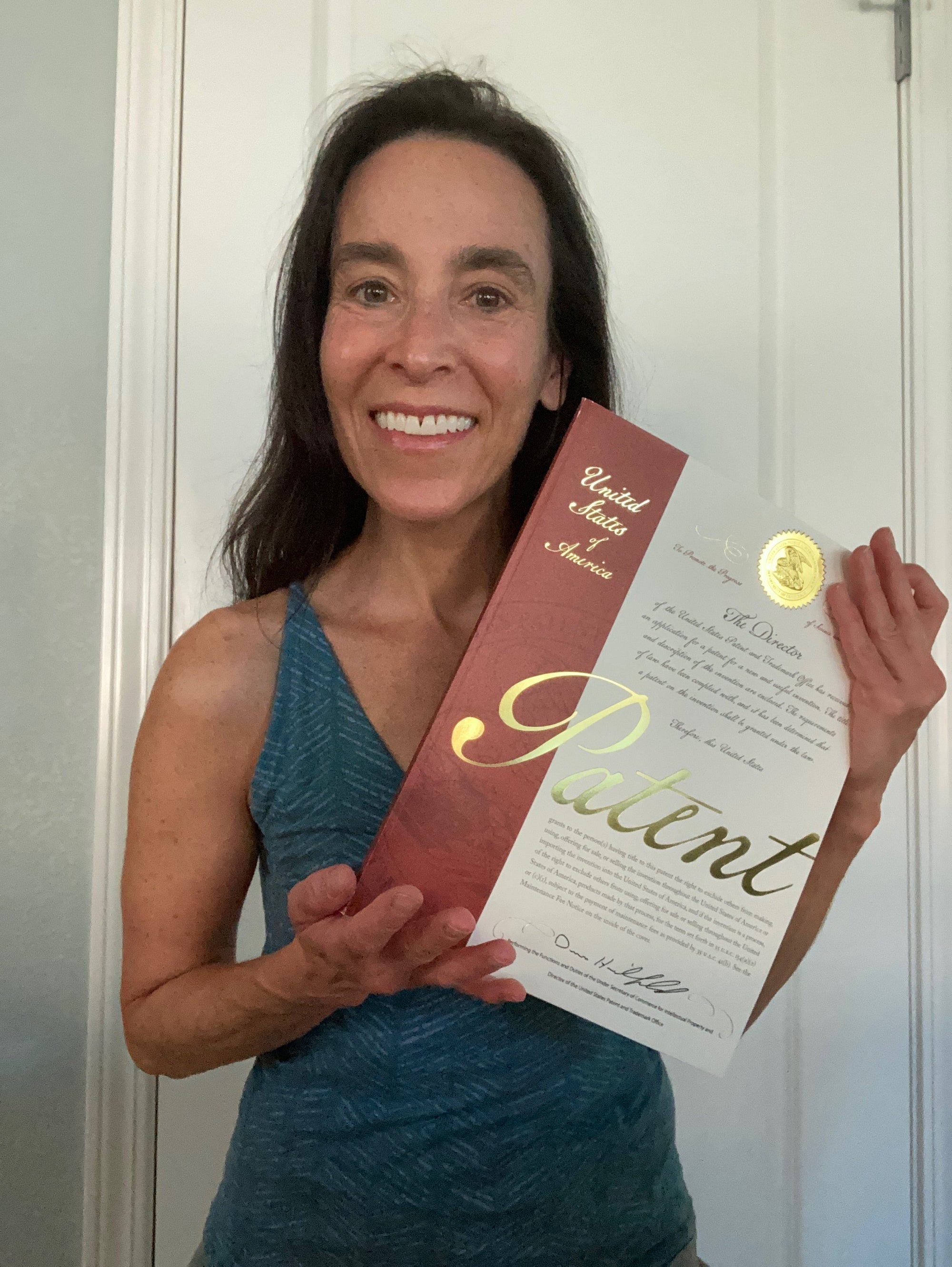 Cyndi Bray stands in a teal shirt holding her utility patent