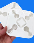 A hand holds two white Wad-Free squares. The product has four tabs with buttons in a keyhole shape and has the logo embossed on it