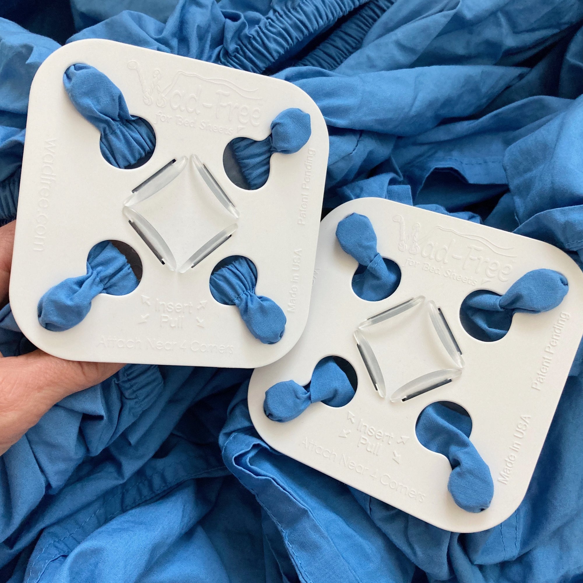 A hand holds a white Wad-Free square attached at four points to a blue fitted sheet, Next to it is a Wad-Free on a flat sheet