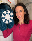 Inventor Cyndi Bray showing Wad-Free for Blankets and Duvet Covers in dryer She wears a bright red sweater and holds a teal blanket attached to a white round Wad-Free