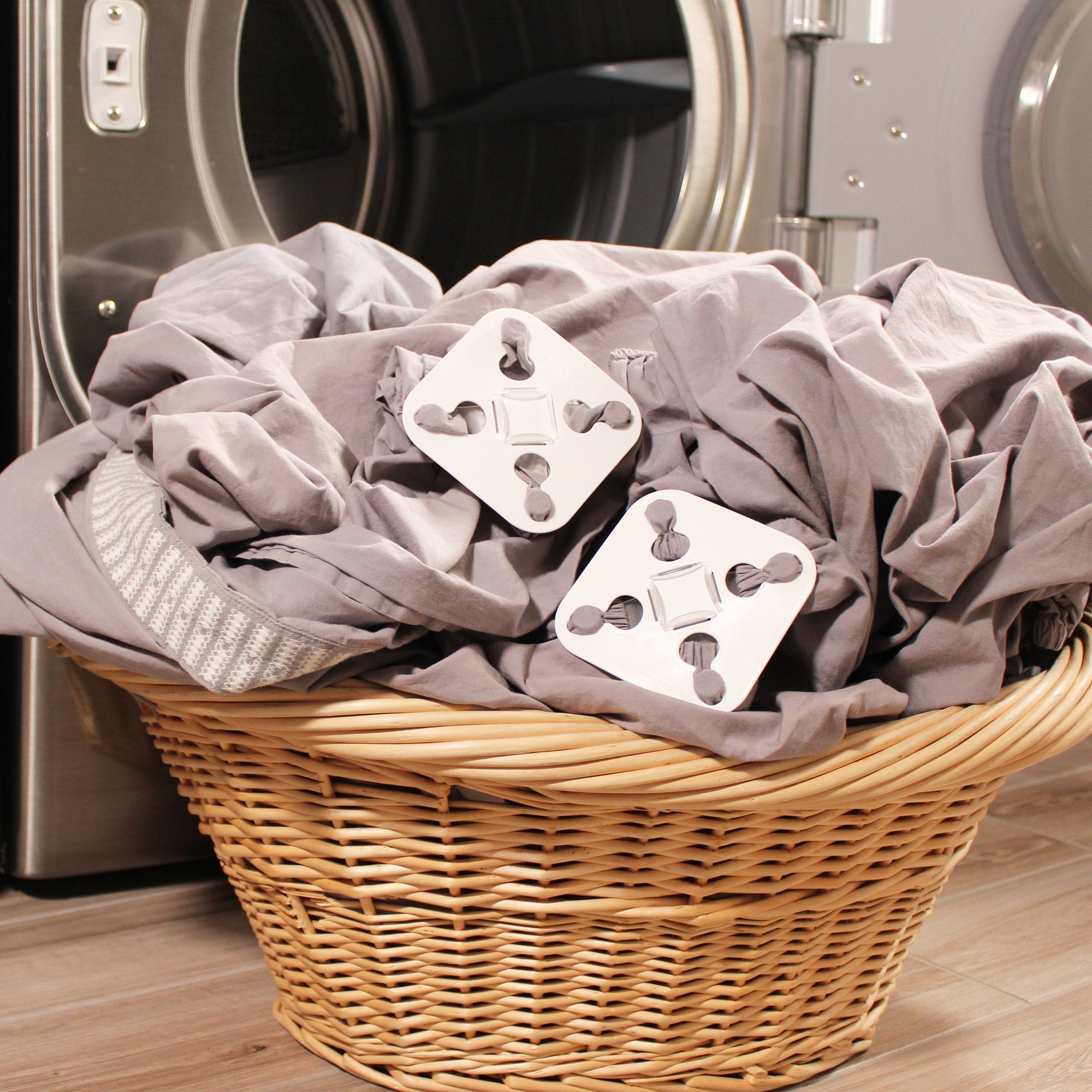 Two grey sheets attached to two white square Wad-Frees are sitting in a wicker laundry basket