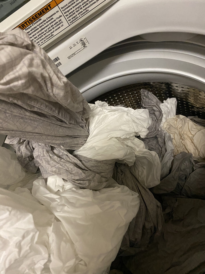 Tangled twisted grey and white sheets being pulled out of an open clothes washer