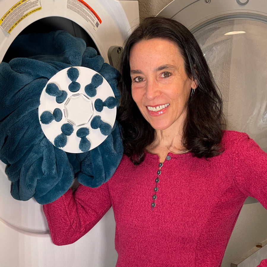 Inventor Cyndi Bray showing Wad-Free for Blankets and Duvet Covers in dryer She wears a bright red sweater and holds a teal blanket attached to a white round Wad-Free