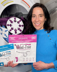 Wad-Free inventor Cyndi Bray in a blue dress holds packaging of Wad-Free for Bed Sheets and  Wad-Free for Blankets and Duvet Covers. The packaging is blue and orchid. One white square is seen in the open clothes dryer attached to a blue sheet and one white round Wad-Free is shown attached to a purple blanket in the open clothes dryer 